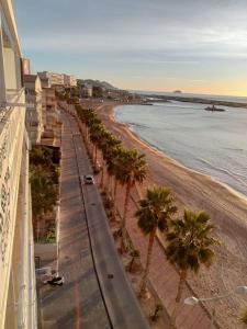 a view of a beach with palm trees and a building at Apartamento L´espigo de Saoret primera linea playa Centro soleado y recien renovado in Villajoyosa