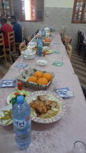 einen langen Tisch mit Teller mit Lebensmitteln und einer Flasche Wasser in der Unterkunft بيت الشباب 22 فبراير ورقلة in Bordj Lutaud