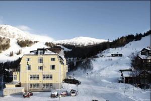Are Alpine Escape Ski-in Ski-out Apt في آرا: مبنى أصفر كبير في الثلج مع سيارات متوقفة