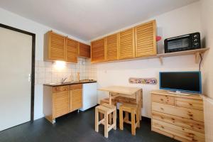 cocina con armarios de madera y escritorio con TV en Lovely 16 m family studio with balcony en Le Monêtier-les-Bains