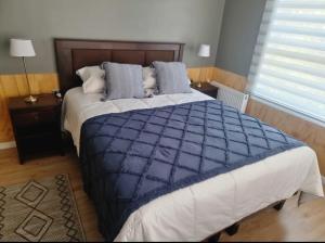 Hostal Callejón Massmann في تيموكو: غرفة نوم بسرير كبير مع بطانية زرقاء وبيضاء