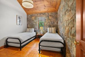 two beds in a room with a stone wall at Breakfast Creek Cottage in Port Fairy