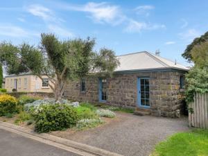 a stone house with a tree in a yard at Breakfast Creek Cottage in Port Fairy
