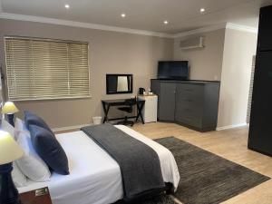 Schlafzimmer mit einem Bett, einem Schreibtisch und einem TV in der Unterkunft Grants Hill Inn in Bloemfontein