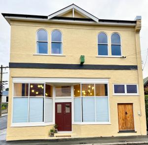 una casa gialla con finestre bianche e una porta rossa di Opoho Heritage Guest Suite a Dunedin