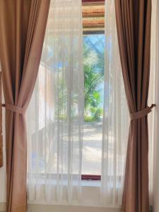 a window with white curtains and a palm tree at Kega Lighthouse Resort Bình Thuận in Ke Ga