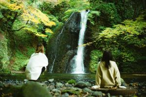 two women sitting in front of a waterfall at Hotel Yutoria Fujisato in Fujisato