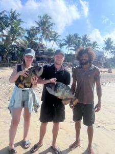a group of three people holding fish on the beach at Ceylon Beach Home in Galle