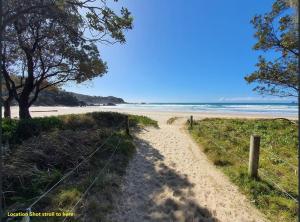 a sandy beach with a fence and trees and the ocean at Beach Haven @ Diggers in Coffs Harbour