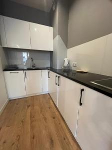 a kitchen with white cabinets and a wooden floor at LubMarex1 Sławińska 508 in Warsaw