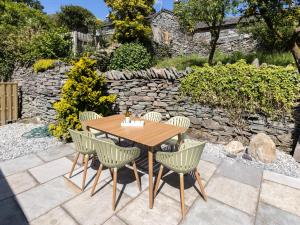a wooden table and chairs on a patio with a stone wall at Langdale Boulders in Ambleside