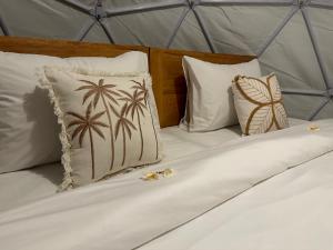 uma cama com almofadas brancas com palmeiras em Glamping @ Pebbles & Fins em Kubu