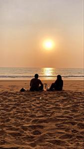 dos personas sentadas en la playa viendo la puesta de sol en Blue Lagoon Redefined, en Gokarna