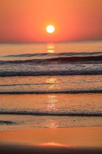 una puesta de sol naranja sobre el océano con olas en Blue Lagoon Redefined, en Gokarna