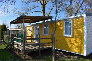 Casa pequeña amarilla con porche de madera en CAMPING LE NAVARRE *** en Vias