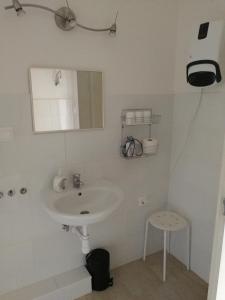 a white bathroom with a sink and a stool at Zsuzsanna Vendégház in Gyomaendrőd