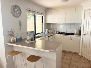 una cocina con armarios blancos y una barra con taburetes en The Scarborough Beach House - Walk to the beach! en Perth