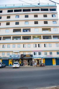 a large white building with a car parked in front of it at Roma Stays - Spacious Studio in Nyali opp Retna Square Close to Nyali Cinemax in Kisauni