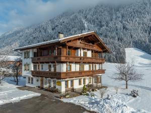 une grande maison en bois sous la neige avec des arbres dans l'établissement Appartements Penzinghof, à Mayrhofen