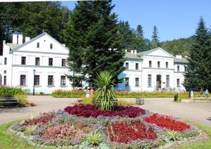 um jardim com flores em frente a um edifício branco em GLORIETTA Apartments & SPA em Iwonicz-Zdrój