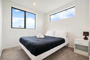 a white bedroom with a bed and two windows at Te Atatu Cozy Brand New House 4 in Auckland