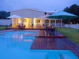a swimming pool with an umbrella and a house at The Dunes Resort - Forest View in Plettenberg Bay