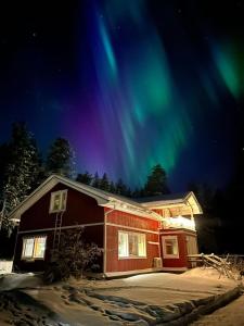 une maison avec l'aurore dans le ciel dans l'établissement Puolukkamaan Pirtit Cottages, à Lampsijärvi