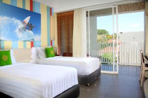 two beds in a hotel room with a surfer on the wave at Bliss Surfer Hotel by Tritama Hospitality in Legian