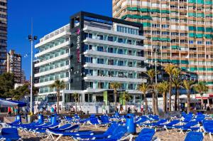 a beach with blue lounge chairs and a building at Hotel Brisa in Benidorm