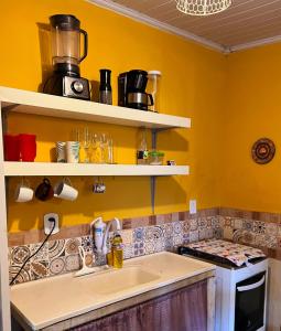 uma cozinha com paredes amarelas, um lavatório e prateleiras em Chalé Maria Bonita - Ilha Grande, RJ em Angra dos Reis