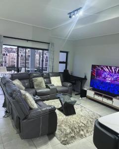 ein Wohnzimmer mit einem Ledersofa und einem Flachbild-TV in der Unterkunft Munyaka Lagoon Penthouse in Midrand