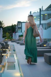 a woman in a green dress walking down a sidewalk at Trypiti Resort Blue Dream Palace and Hive Water Park in Limenaria