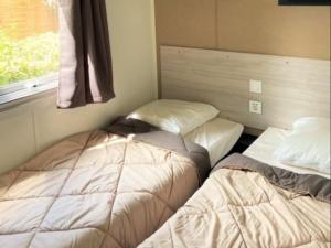 2 camas individuales en una habitación con ventana en Camping Beau Rivage, en Mèze