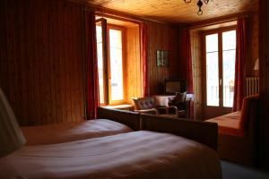 a room with two beds and a chair and windows at Hôtel Hermitage in Evolène