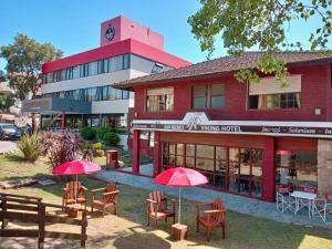 um edifício vermelho com mesas e guarda-chuvas em frente em San Remo Viking Hotel em Pinamar