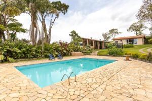 una piscina con due sedie e una casa di chácara paraíso tropical a Biritiba-Mirim