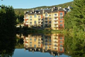 um grande edifício de apartamentos com o seu reflexo na água em BONDURANT 95-15 / Luxury 3 bdr on the village em Mont-Tremblant