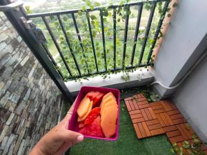 a person holding a pink bowl of fruit on a balcony at Studio Healing at Sayana Apartemen Harapan Indah Bekasi 
