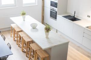 a kitchen with a large white island with wooden stools at The Wagon Shed Stylish Conversion with Garden and Parking in Sowerby Bridge