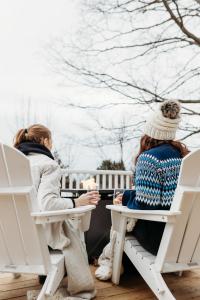 twee vrouwen aan een tafel op stoelen op een veranda bij Lakeview Luxury Farmhouse Retreat - Hot Tub - Games Room in Cobourg