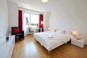 a white bedroom with a large bed and a chair at CITY STAY - Forchstrasse in Zurich