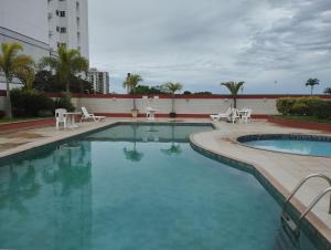 uma grande piscina com cadeiras e mesas brancas em flats aconchegantes piscina e academia via park em Campos dos Goytacazes