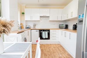 a white kitchen with white appliances and a wooden floor at Cosy 3 Bedroom House with Free Parking and Garden in Earley