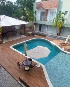 a swimming pool with an umbrella and a table at Vilage Aconchegante - Imbassaí in Imbassai