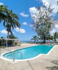 a swimming pool with palm trees and the ocean at Modern 1 Bedroom Apartment - 3 min walk to beach in Saint James