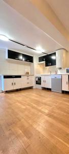 a large kitchen with white cabinets and a wooden floor at L'adorable Maison des Clients 15min de Paris in Houilles