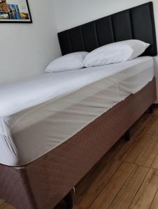Una cama con sábanas blancas y almohadas. en HORTA DO TOMATE, en Bombinhas