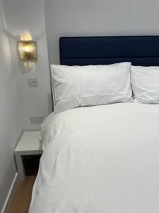 a white bed with a blue headboard and a side table at Novanik Studio Apartment in Milton Keynes
