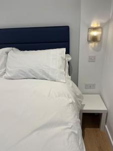 a white bed with a blue headboard and a table at Novanik Studio Apartment in Milton Keynes