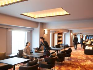 Dos personas de pie en una habitación con mesas y sillas en RIHGA Royal Hotel Osaka, en Osaka